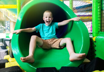 Fototapeta na wymiar Portrait of blond boy who plays in play area. Children labyrinth. Close-up of the face, on which emotions of happiness, fun and carelessness. Hill, labyrinth, trampoline. Safe attraction for children