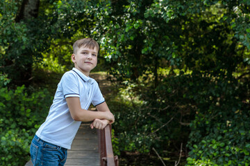 Naklejka na ściany i meble A boy standing on a bridge in the forest and looking at the camera with a smile. Rest in the village. Space for text.