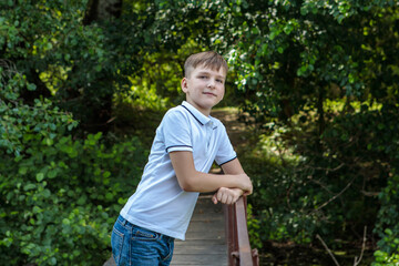 A boy standing on a bridge in the forest and looking at the camera with a smile. Rest in the...