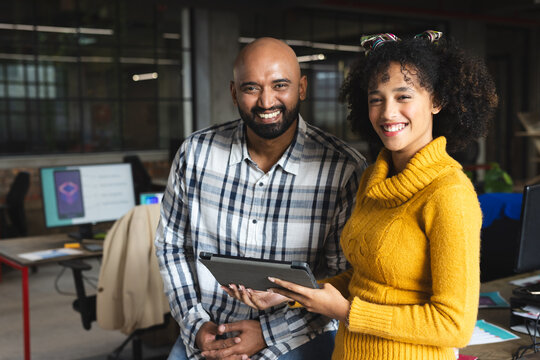 Portrait of happy diverse female and male colleagues with tablet smiling in office