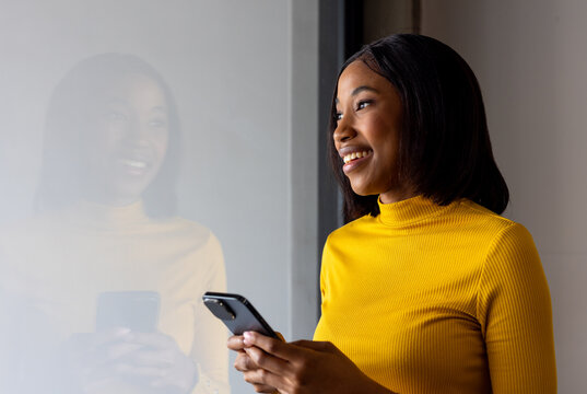 African american businesswoman using a smartphone near a window at modern office, copy space