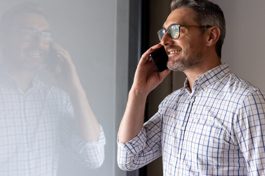 Caucasian businessman talking on smartphone near a window at modern office, copy space