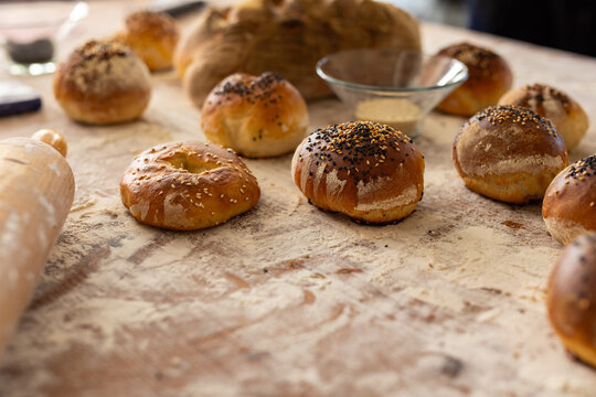 Close up of roller and fresh rolls with seeds on countertop with flour in bakery kitchen, copy space