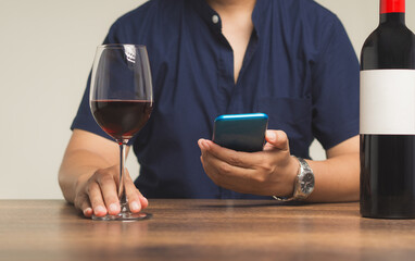 Close-up of hands holding a glass of red wine and a smartphone while sitting at the table.
