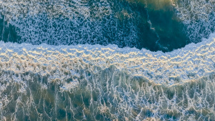 Waves crashing onto a sandy shoreline with bright white foam during sunset creating a tranquil coastal atmosphere