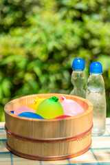 木桶に入れられた水風船と冷えた瓶ラムネ / 夏休み・昭和レトロ・日本の夏の水遊びのイメージ