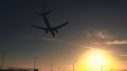 Airplane flying against a sunset sky with vibrant colors illuminating the horizon