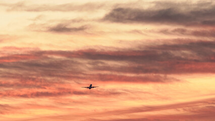 Airplane flying across a vibrant sunset sky with colorful clouds in the evening hours over a scenic landscape