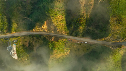 Stunning aerial view of a winding road through lush green hills surrounded by mist during sunrise