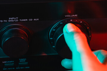 A woman's hand turns on and increases the volume of music on the amplifier. Colorful neon light....