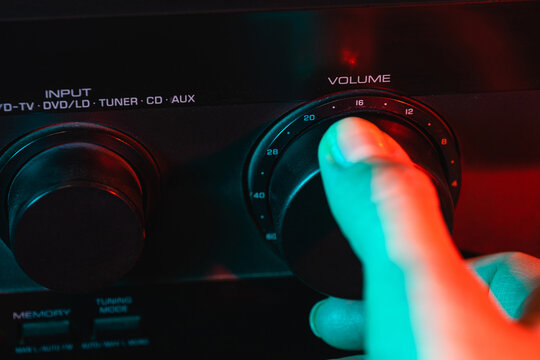 A woman's hand turns on and increases the volume of music on the amplifier. Colorful neon light. Macro view. Close-up of volume controls panel. Audio Receiver Control Panel. Control panel by sound amp