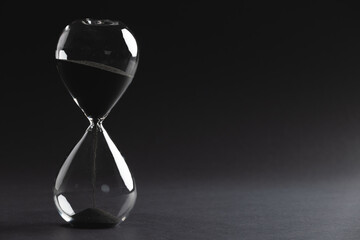 Close up of hourglass with black sand and copy space on black background - obrazy, fototapety, plakaty