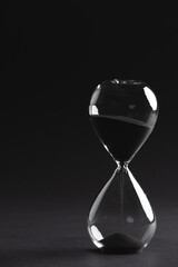 Close up of hourglass with black sand and copy space on black background