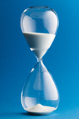 Close up of hourglass with white sand and copy space on blue background