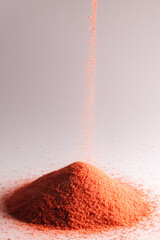 Close up of orange sand pouring into heap and copy space on white background