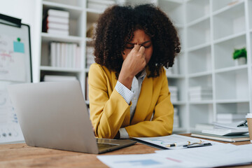 Burnout American African business woman in stress works with many paperwork document, migraine...