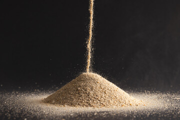Close up of sand pouring into heap and copy space on black background © vectorfusionart