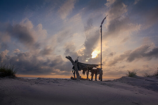 A makeshift, wooden shack is silhouetted against the morning sunrise at a beach. 