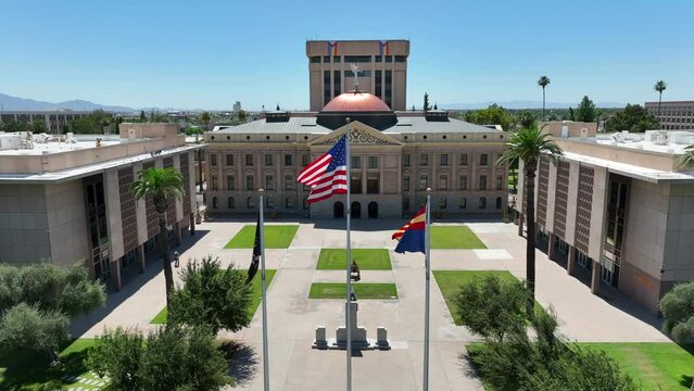American flag and Arizona State flag waving in Phoenix, AZ at capitol building. Cinematic aerial establishing shot of government building.