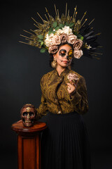 Portrait of woman in sugar skull makeup holding a skull . Halloween and day of the dead makeup. Catrina portrait.