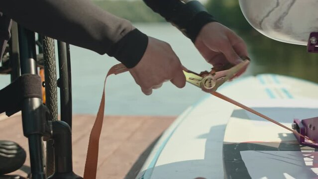 Cropped shot of unrecognizable wheelchaired man in wetsuit checking safety seatbelt on his adaptive supboard before going on water