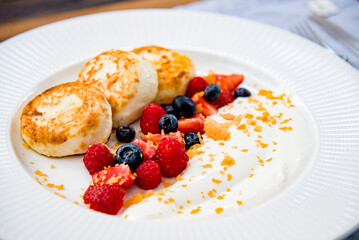 healthy breakfast with cottage cheese pancakes with berries and cream on white plate