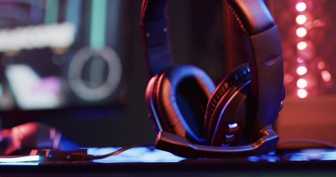 Video of headphones, computer and gaming equipment on desk with copy space on neon background