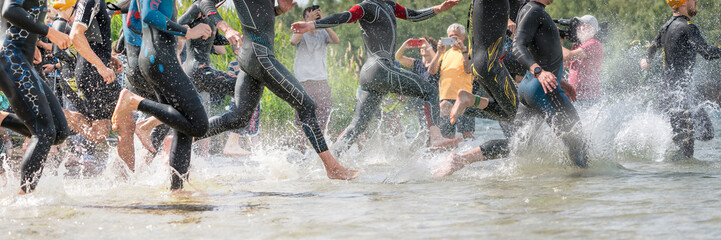 Athletes in wetsuits running into a lake at a triathlon competition