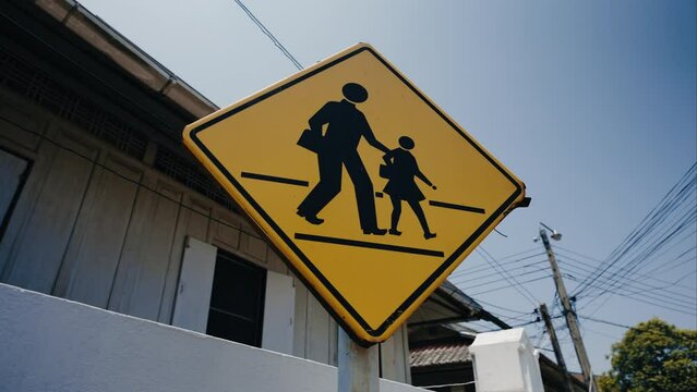 Caution school zone yellow road sign with symbol of parent and child togeather in city district. Dolly moving camera shot