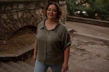 Portraiy of a beautiful girl is wearing a khaki t-shirt, the overweight woman posing against stone biege wall. The fashion outfit for plus-size woman for the city, minimalizm urban style clothes