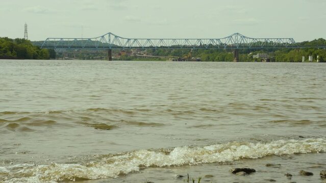 waves crashing the shore of the Ohio river with Rochester Monaca bridge in the background on an overcast day