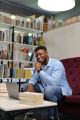 African guy works in the library on a laptop, vertically.