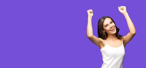 Fototapeta na wymiar Photo of happy gesturing beautiful woman rising hands up with clenching fists, in white smart casual clothing, isolated on violet purple color background. Excited brunette girl at studio.