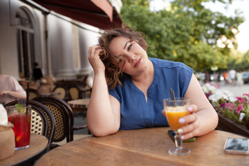 Beautiful young woman sit in cafe with glass of cooly drink. Plus size woman  drink red juice and smiling