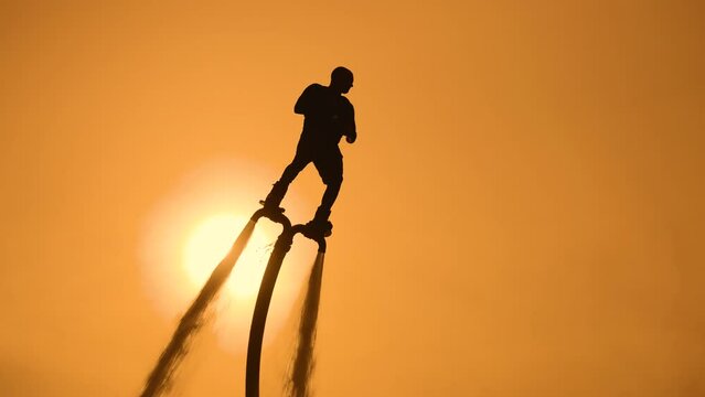 Epic scene at sunset. Silhouette of a flyboarder against the backdrop of the setting sun and sky. The athlete does somersaults in the air
