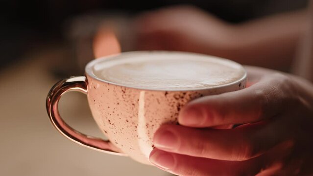 Female hand holds a beautiful cup of freshly made cappuccino coffee with foam. Extreme close up macro shot