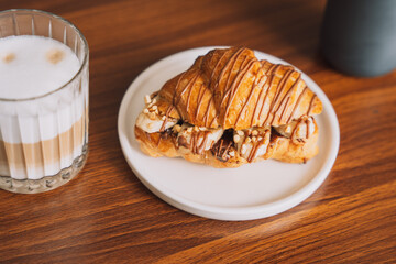 Croissant with chocolate and banana inside on a white plate with a cup of coffee.