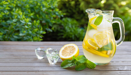 Lemonade pitcher with lemon, mint and ice on garden table. View with copy space