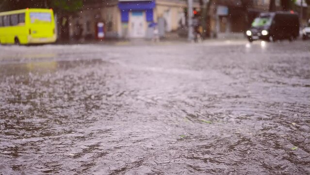 Slow motion, Swift stream of rainwater flows into storm drain, cars are driving at city crossroads on background. Heavy rain leads to sewage overflow, flood in city