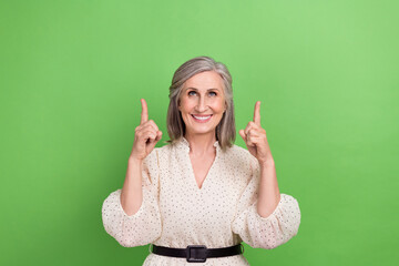 Photo portrait of beautiful grandma fingers point look up empty space wear trendy white outfit isolated on green color background