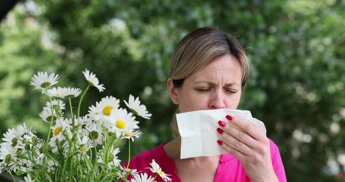 Woman with spring fever blows her nose in a napkin near chamomile flowers. Allegy to flowers