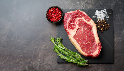 Ribeye fresh raw beef steak with spices on stone board. Top view flat lay with copy space