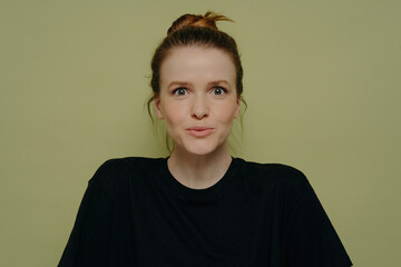 Wide-eyed woman in black tee, hair in bun, expressing surprise, staring at camera on green backdrop.
