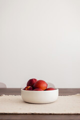 Ceramic bowl of fresh red nectarine fruit with copy space on white kitchen wall on wooden table. Modern design apartment.