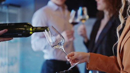 Close-up of an unidentified waiter pouring wine into a glass at a tasting. A young woman picks up a glass with a drink in the interior of a restaurant