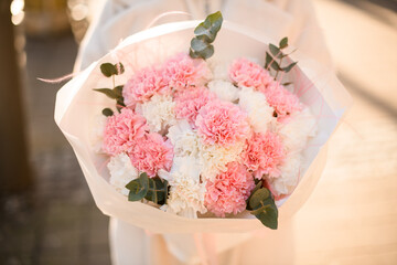 Bouquet of pink, white carnations and eucalyptus branches formed in white craft paper in woman's hands