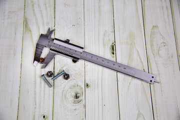 A metal caliper with nuts and bolts on a gray wooden table. Tools, construction, production, design, structures.