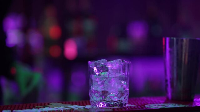 4K Professional male bartender pouring mixed blue liquor cocktail drink from cocktail shaker into shot glass on bar counter at nightclub. Mixologist barman making alcoholic drink serving to customer