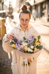 Fototapeta premium Young woman wearing white coat holding luxurious flowers mix in wrapping paper