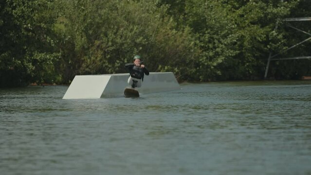Cheerful Caucasian teenage boy with no legs sitting in adaptive wake board and surfing in river pulled by boat with rope